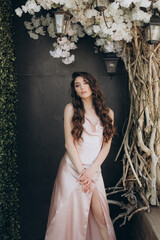 Beautiful, stylish, and elegant girl brunette, model, with makeup and curly hair in a peach-colored silk dress for a magazine photoshoot in fashion style.