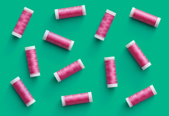 A flat lay pattern of spools of pink thread on green background. Top view