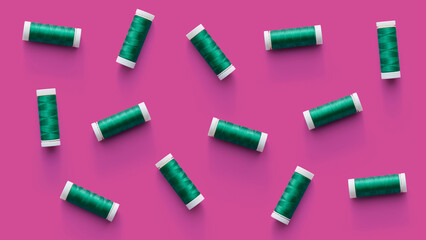 A flat lay pattern of spools of green thread on pink background. Top view