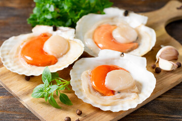 Raw scallop in the shell on a serving board on a brown wooden table 