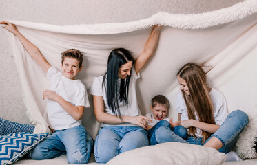 happy family mom and small children laughing merrily sitting on the sofa covered with a white blanket