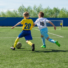 Obraz premium Children's football. An interesting football moment at the match and training. The active struggle and dynamics of the boys' soccer match. The boys are recklessly fighting for the ball