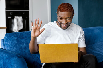 Happy male freelancer using laptop, waving hello to coworkers at video meeting, smiling. Successful businessman having an online conference with colleagues, discussing a project, distant work concept
