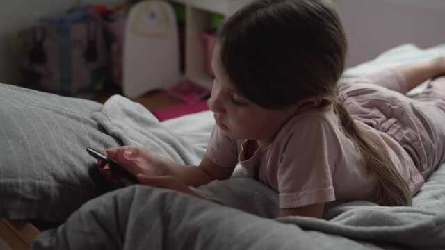 Girl with ponytail lying on bed playing game on smartphone