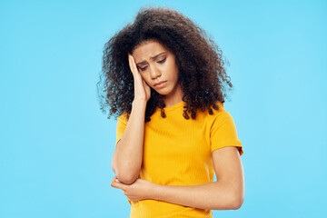 upset woman with curly hair in a yellow t-shirt on a blue background