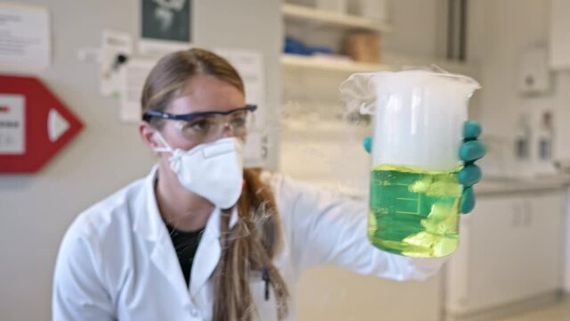 Scientist in protective clothing watching liquid in laboratory beaker