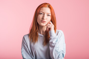 Portrait of a redhead pensive girl in the studio on a pink background