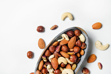 Different types of nuts in a ceramic snack plate and scattered on isolated white background. Nutrient dense vegan snacks. Clean eating concept. Close up, copy space for text, top view, flat lay.