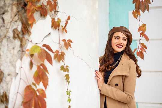 Fashionable woman in leather brown beret and beige caot outdoors in autumn