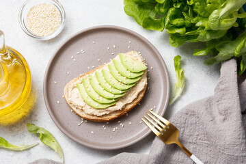 Fototapeta na wymiar Open sandwich with chickpea hummus and avocado on white stone table background. Healthy food, avocado toast for breakfast or lunch. Flat lay, top view