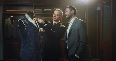 Cinematic shot of young handsome man is trying his new custom tailored suit with designer in a...