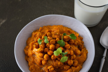Thick pumpkin soup with baked chickpeas and radish sprouts in a plate with a glass of milk on the table, delicious healthy dinner