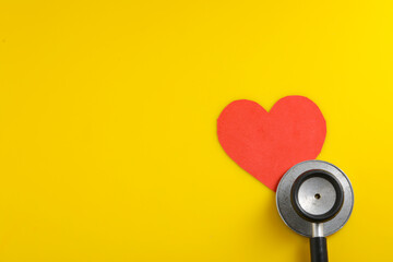 A heart with a stethoscope on yellow background.