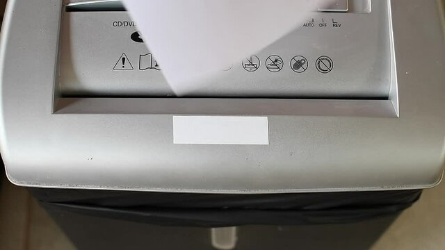 Shredding paper with an electric paper shredder. The machine is sucking the paper and cutting it into pieces. The concept is to preserve the environment, reduce pollution and the greenhouse effect.