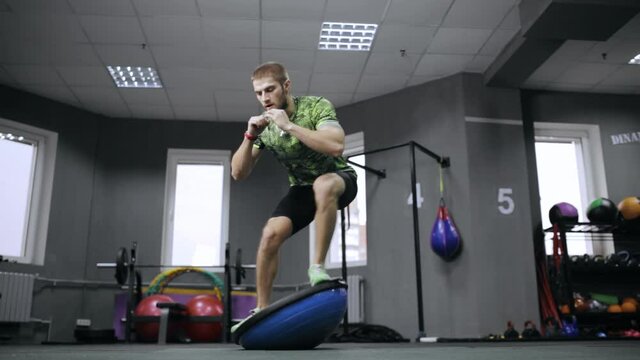 From below of active male athlete doing exercises on balance bosu ball during dynamic workout in modern gym 