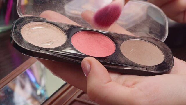 Female hands applying make-up blush from face cosmetic palette close up