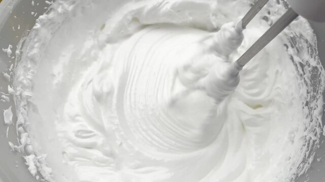 Beaten egg white. Whipped cream white in bowl and mixer, top view.