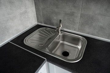 Stainless steel kitchen sink on a dark grey granite worktop. Kitchen sink and water tap in the kitchen.