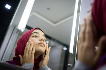 Muslim beautiful girl looking into mirror checking face 