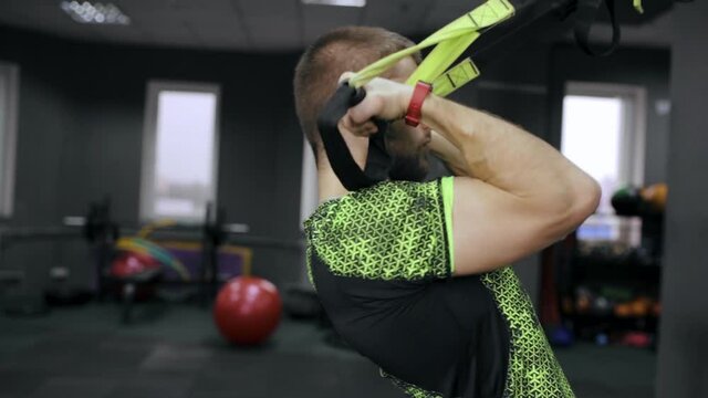 Side view of strong sportsman doing exercises with TRX straps during suspension training in gym 