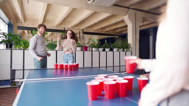 Group of young people playing beer pong in a large room
