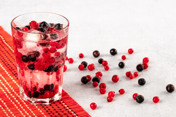 Summer cold drink with water, ice and multicolor berries. A glass of red and black currants on a gray background. Fruitarianism, veganism concept. Vegetarian diet. Berry refreshing lemonade.