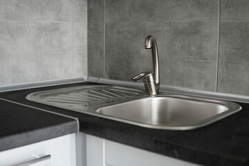 Stainless steel kitchen sink on a dark grey granite worktop. Kitchen sink and water tap in the kitchen.