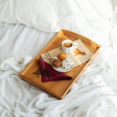 Serving tray with sweet dessert and cup of coffee in bed, white sheets, and blanket in the hotel. Romantic start of the day, coffee in bed with organic dessert.