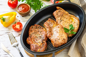 Barbecues parties menu. Baked meat pork loin on the bone with spices in a cast iron pan on rustic wooden table.