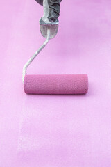 Woman painting a piece of furniture with a paint roller in malva color