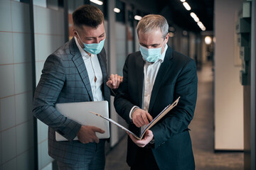Business partners in medical masks discussing project in corridor