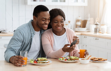 Obraz na płótnie Canvas Romantic African American Spouses Checking New App On Smartphone During Breakfast