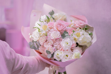 A man's hand holds a lush bouquet of light pink, white cute delicate small roses of different sizes, flowers of green leaves. Paper packaging. Romance.