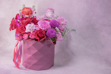 A lush bouquet of red, light pink, purple, white cute delicate small roses of different sizes, flowers in round paper box with geometric pattern. Place for text