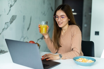 Image of a beautiful young woman at the kitchen indoors at home using laptop have a dinner watch videos.