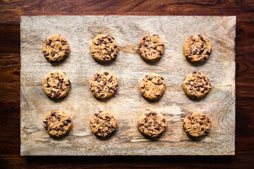 Freshly baked chocolate chip cookies on a wooden board on dark and moody wooden background