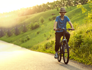 Naklejka premium teenager riding a bicycle on the road summer sunlit, bike ride
