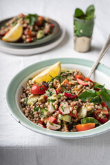 Side view of two bowls with healthy vegan wholewheat pearl couscous salad with mint tea on a white background, with copy space