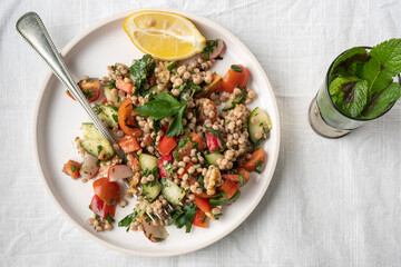 Flat-lay of a single plate of a healthy vegan wholewheat pearl couscous salad on white plate and white background, flatlay