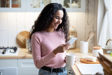Mobile Communication. Young Beautiful Woman Using Smartphone And Drinking Coffee In Kitchen