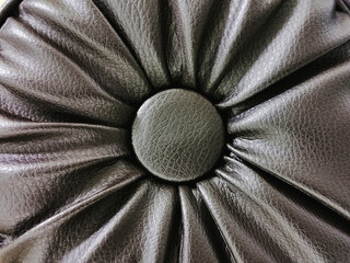 Close up detail of genuine dark brown leather buttoned with deep centered pleat pattern. Luxury style upholstery  element and texture for interior or furniture design, Selective focus image.