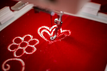 Machine embroidery of flowers with silver thread on red velvet fabric.