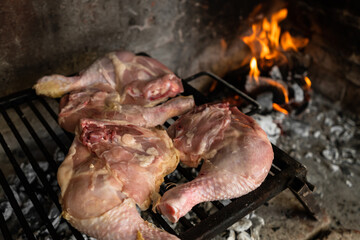 Chicken quarters on the grill with embers and a fire in the background. Argentinean "asado" concept.
