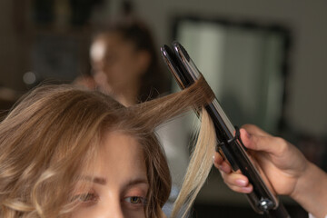 Fototapeta premium Hair stylist making hairdo with styling iron