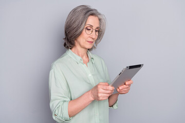Naklejka premium Photo of serious focused concentrated mature businesswoman working in tablet isolated on grey color background
