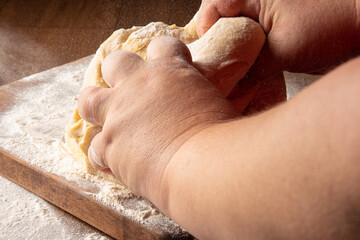 Dough being kneaded by hands and sprinkled with wheat on wood, selective focus.