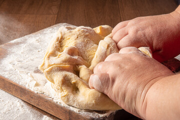 Fototapeta na wymiar Dough being kneaded by hands and sprinkled with wheat on wood, selective focus.