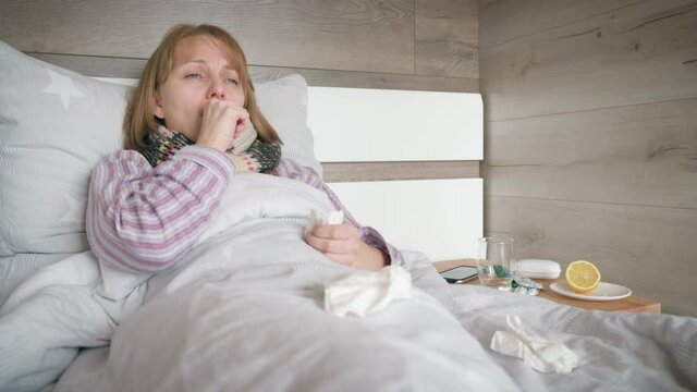 Sick woman touch neck in bed coughing. She feels sore throat. Unhealthy ill caucasian woman at home. Self isolation at covid-19 quarantine. Adult female suffering from flu or coronavirus. 