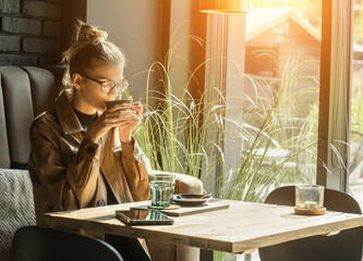 Young woman drinking coffee cup and sitting in cafe. Girl in glasses pauses after work.
