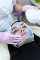 The beautician in a white medical gown washes off the cosmetic mask from the client's face. Beautiful woman with cosmetic facial mask in the spa salon. Woman having a cosmetic face mask.